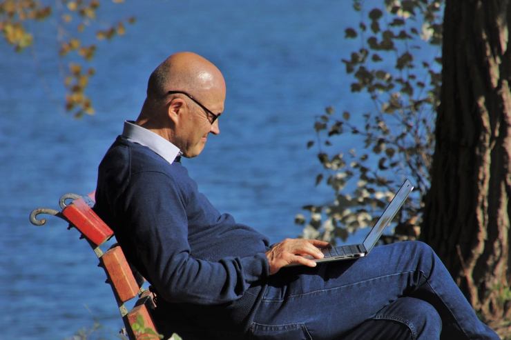 pensionato al pc seduto su panchina in riva al lago