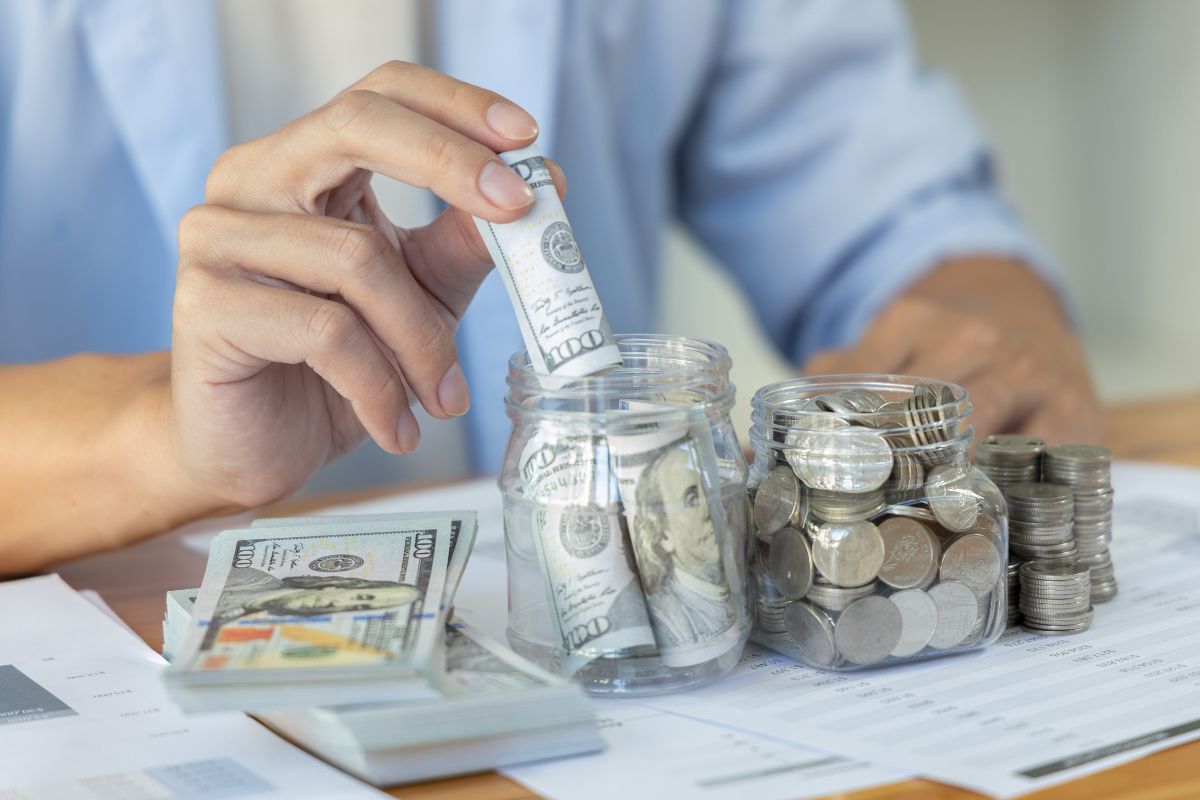 Persona che mette dei dollari in un vasetto di vetro