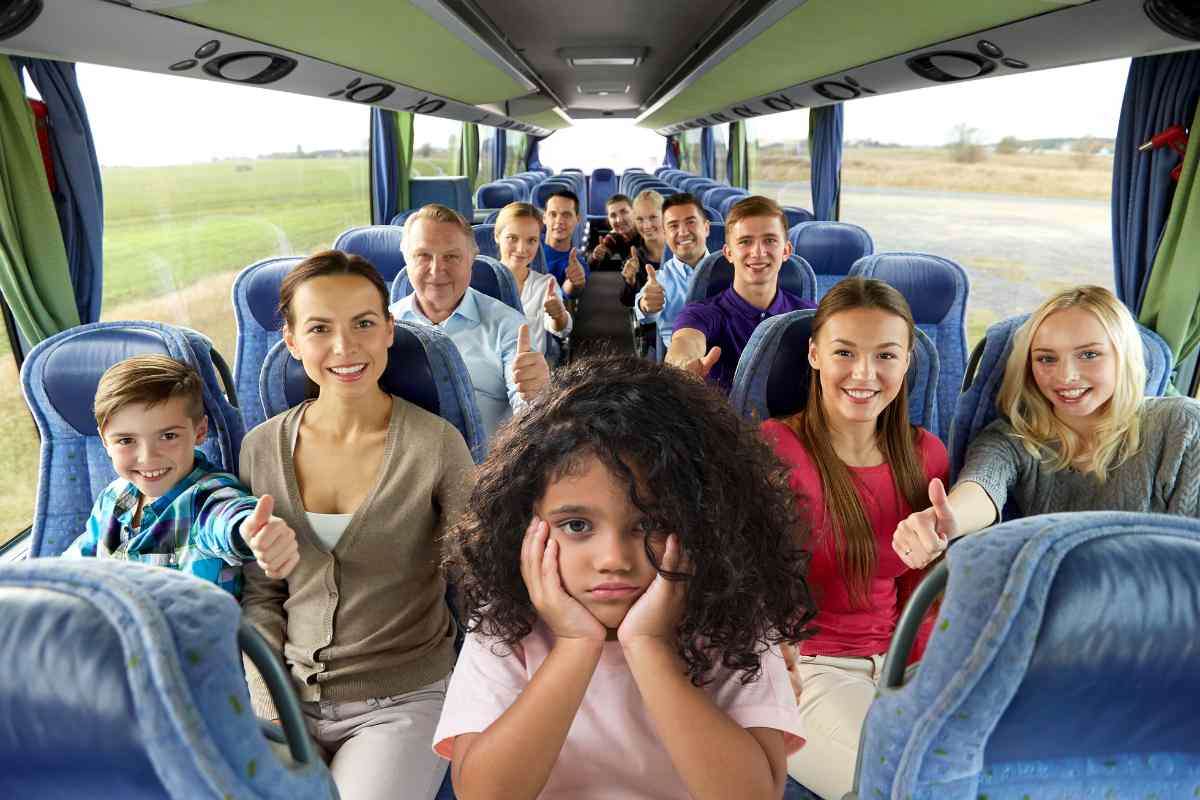 insegnanti e allievi sorridenti su autobus e una bambina triste in primo piano