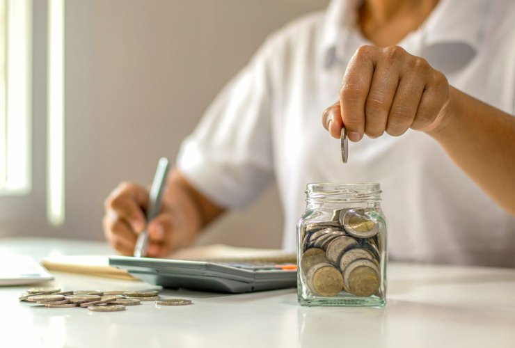 Persone che fa dei calcoli e mette monete in un vasetto di vetro