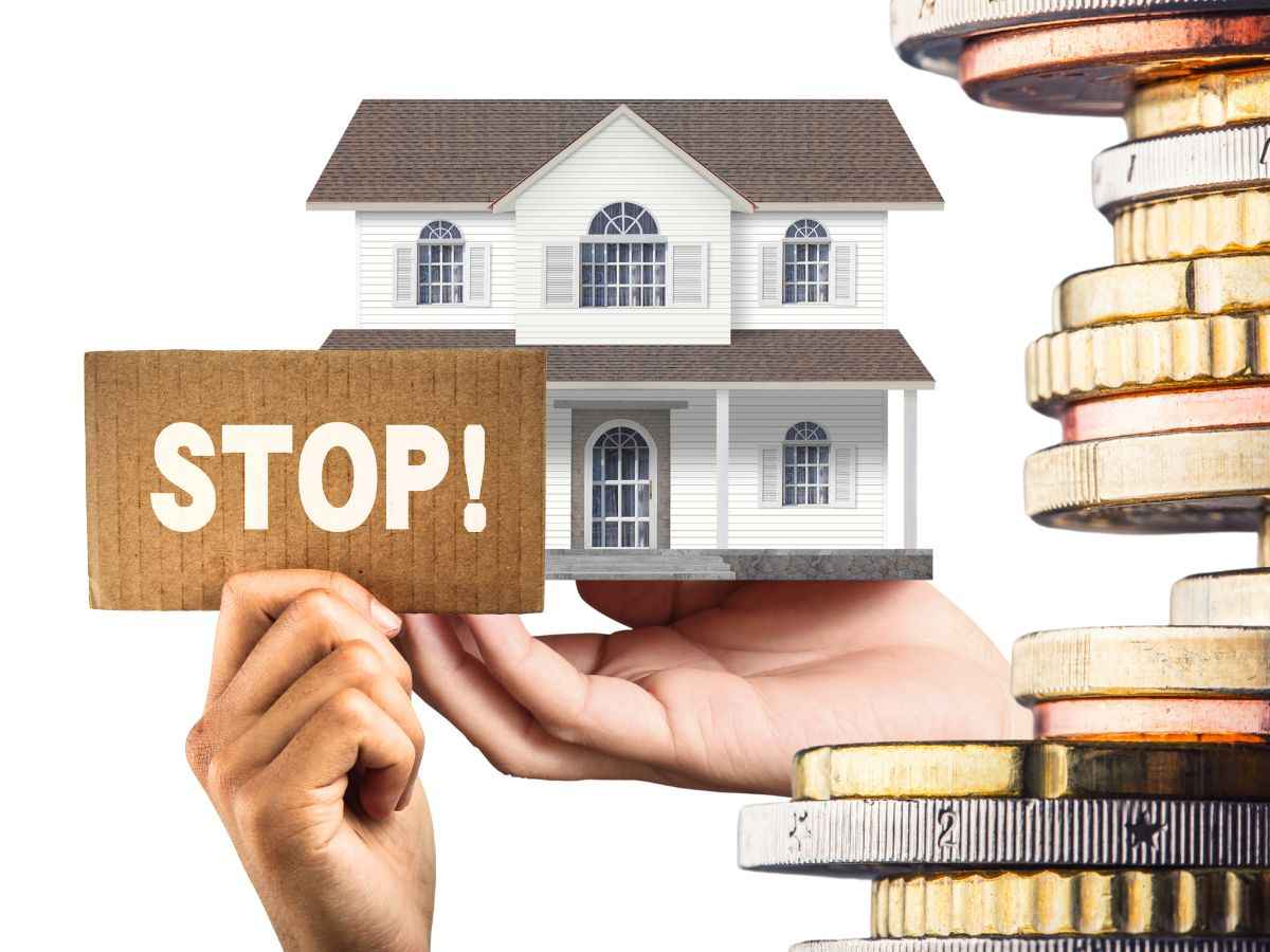 sfondo miniatura casa con monete euro e cartellino in mano con scritta stop