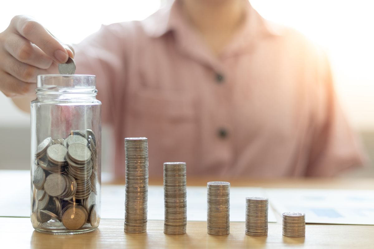 Persona che conta dei soldi e li mette in un contenitore di vetro