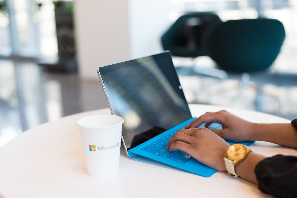 Persona che scrive al pc e bicchiere con logo Microsoft