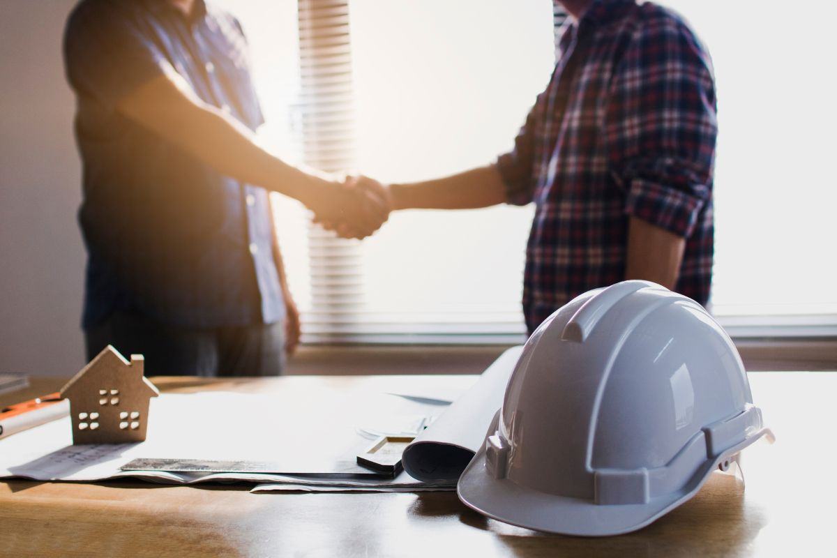 Persone che si stringono la mano dopo aver completato dei lavori e cappello da lavoro