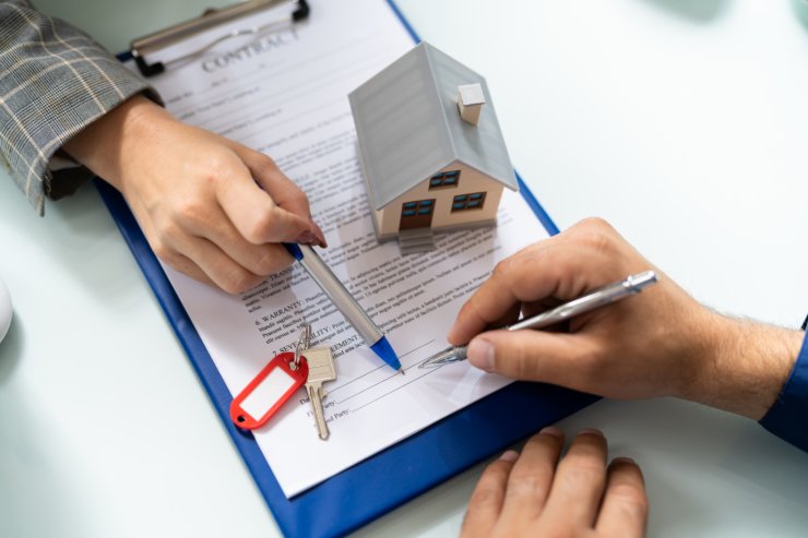 mano con penna che sta per firmare documento casa in miniatura e altra mano che indica dove firmare