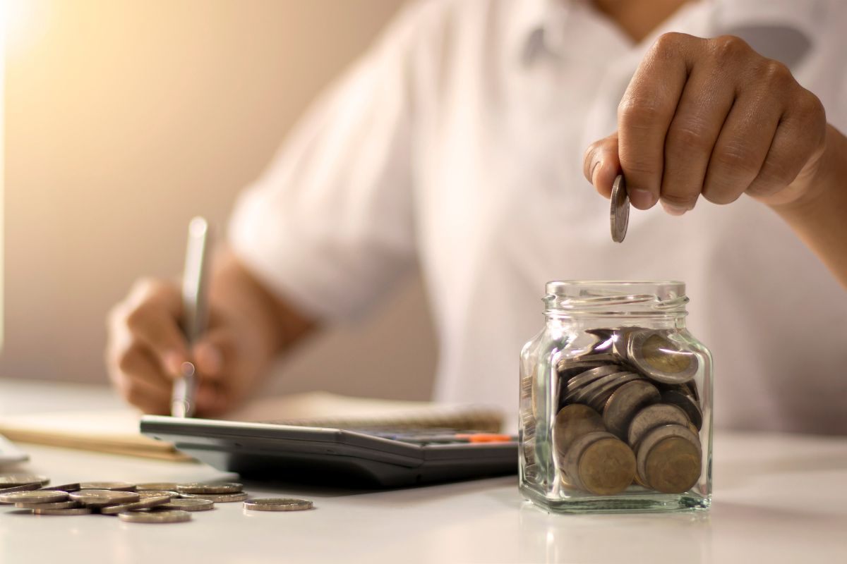 Persona che fa dei conti e mette una moneta in un vasetto di vetro
