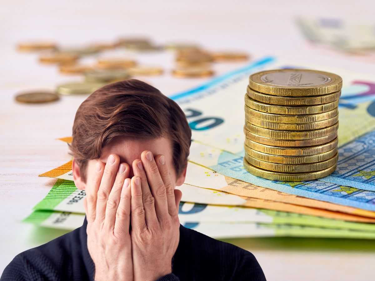 sfondo banconote e monete euro e uomo con mani in faccia disperato
