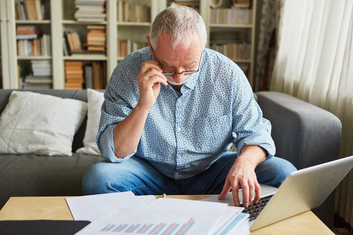 pensionato con occhiali guarda preoccupato documenti