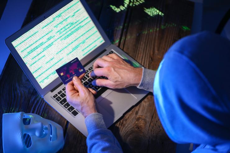 uomo al pc con carta in mano e maschera truffatore