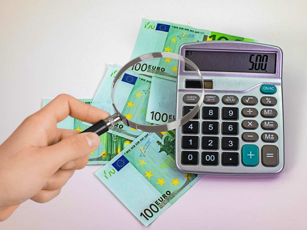 sfondo calcolatrice e banconote euro e mano con lente di ingrandimento