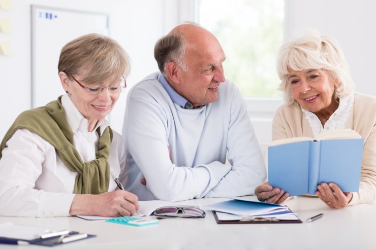 tre pensionati sorridenti un uomo e due donne davanti a libri e documenti