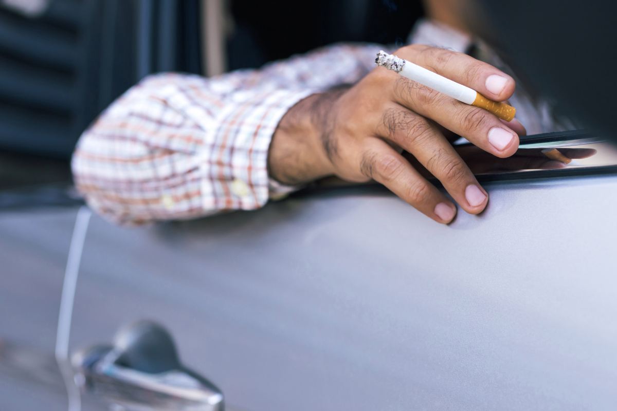 uomo guida con braccio fuori dal finestrino e sigaretta