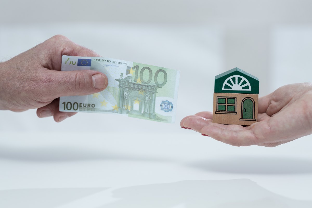 una mano tiene casa in miniatura un'altra una banconota da 100 euro