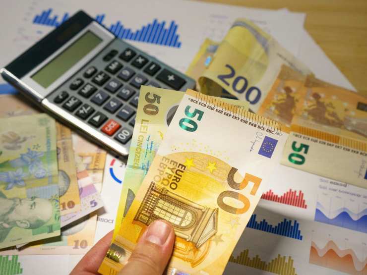 calcolatrice, banconote euro e mano che ne tiene alcune 