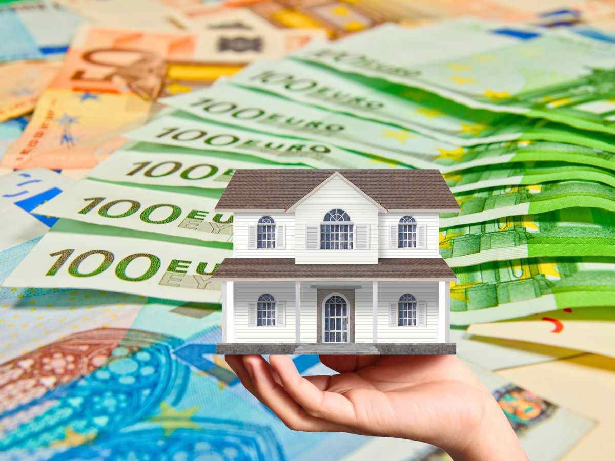 sfondo banconote euro e casetta in miniatura in mano