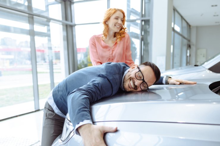 uomo felice abbraccia auto nuova e compagna sorride