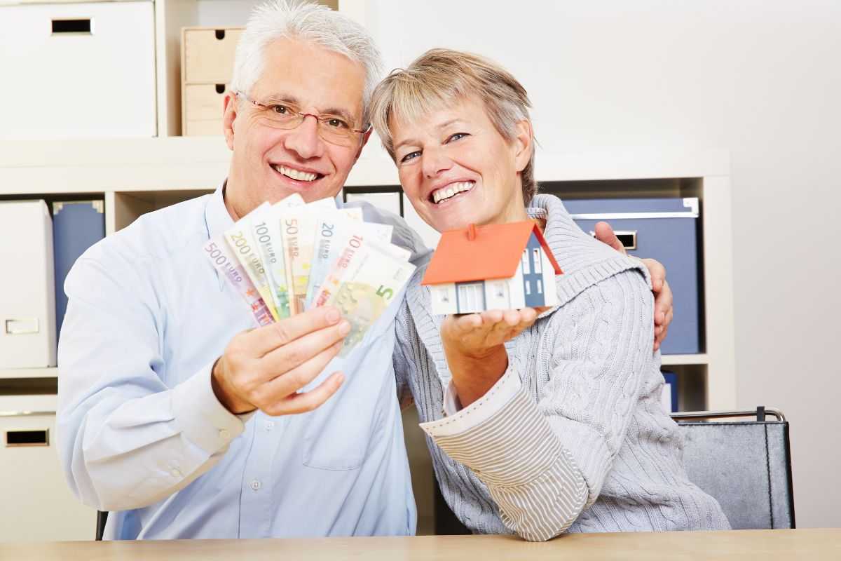 persone felici per il bonus sociale con banconote in mano e la miniatura di una casa