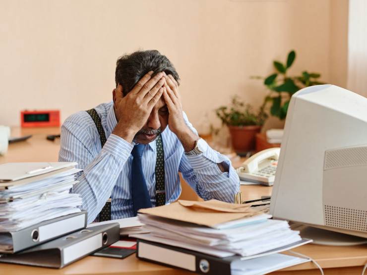 uomo disperato alla scrivania con pc e documenti 