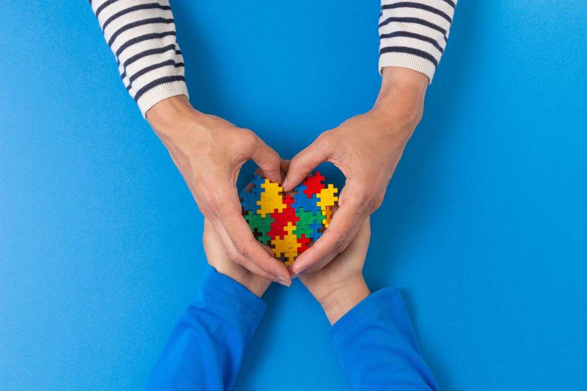 mamma che tiene le mani al figlio e insieme un puzzle a forma di cuore