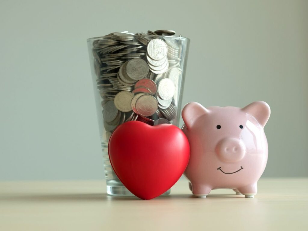 Bicchiere pieno di monete, salvadanaio e cuore